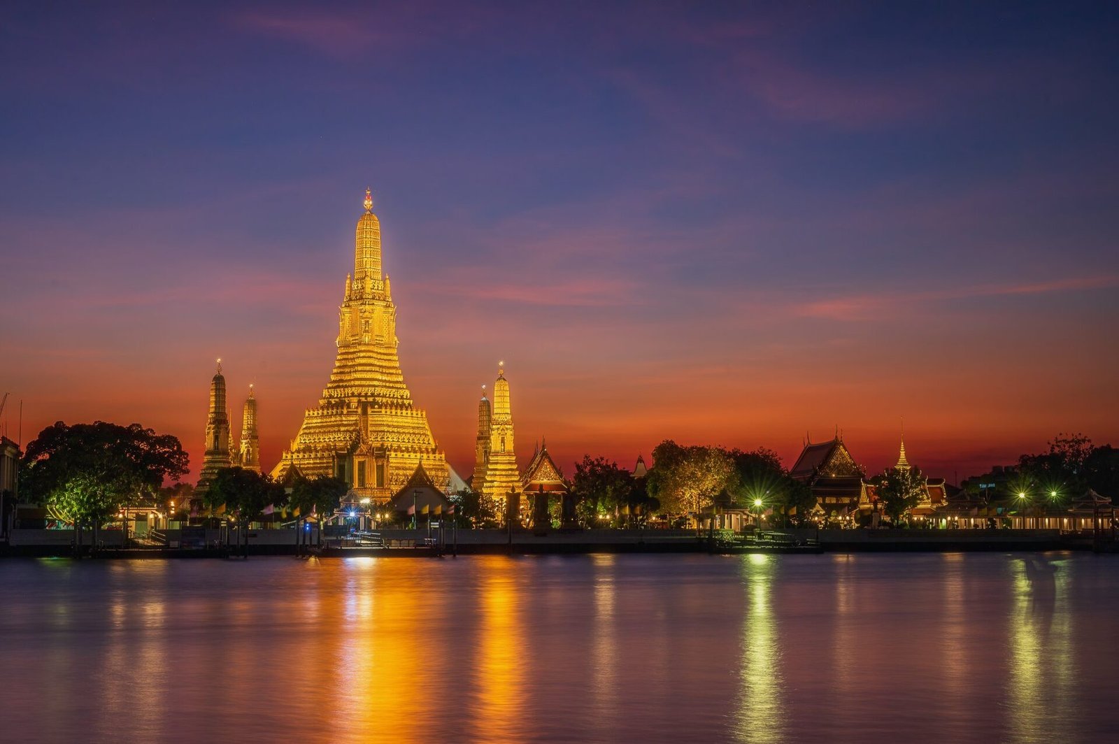 Wat Arun temple illuminated at sunset across the Chao Phraya River
