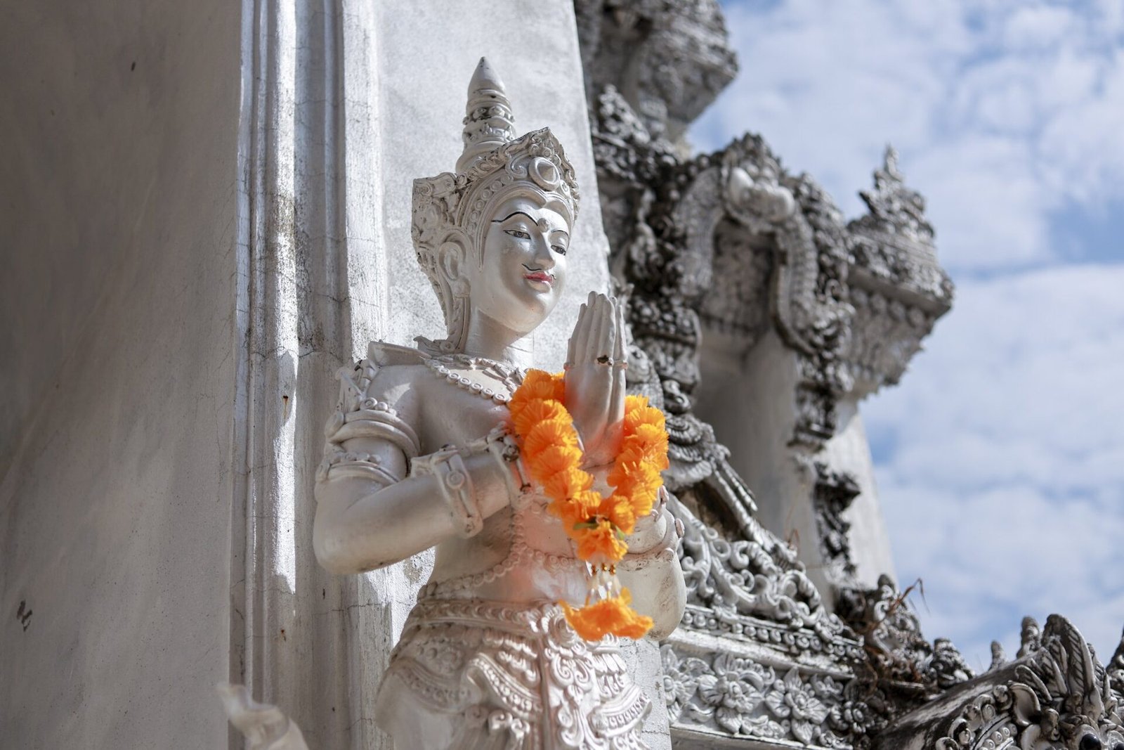 White temple guardian statue in wai gesture adorned with marigold garlands